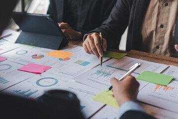 Groups of businesspeople working together as a team of analytics point to company graphs and charts to compare marketing strategies for new product offerings.