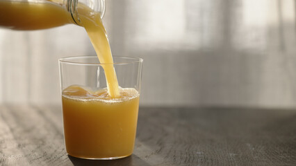 pour orange juice in tumbler glass on oak table with copy space
