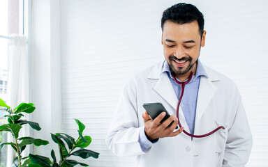 Portrait Asian handsome male doctor with beard wearing white ground uniform, holding stethoscope, smiling with kindness, happiness, posing with copy space. Health and Medical Concept