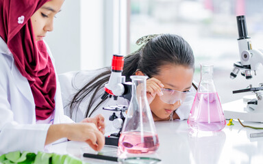 Selective focus teenage asian student girl wearing white gown, smiling with fun, studying chemistry, biochemistry, doing experiment in science class at school, looking at test tube. Education Concept.