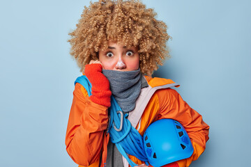 Amazed scared female alpinist feels cold while climbing mountain wears warm scarf windbreaker...