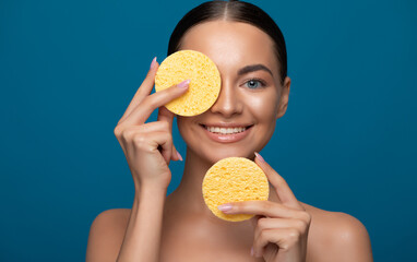 Young female model holding yellow sponges near her face.