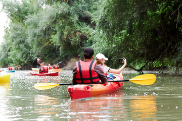 Woman taking a selfie with a smartphone during floating on kayak. Man and woman in red kayak. Concept of rest, leisure and family vacation