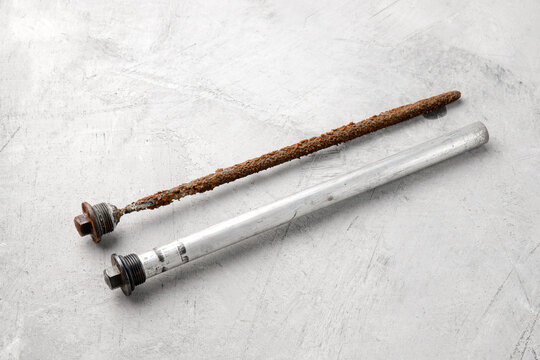 New and old magnesium anode to protect an electric water heater from rust on a gray concrete background, close-up.