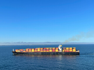 Large container ship smoking a lot during moving to the port