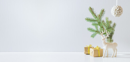 Christmas, New Year home decor. Empty white wall mock up with green fir branches in a vase, deer and gift box on a white table. Mock up for displaying works