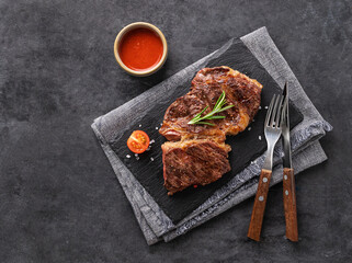 BBQ grilled beef steak with sauce,tomatoes and rosemary on black slate on dark  background.