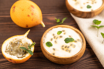 Yoghurt with granadilla and mint in wooden bowl on brown wooden, side view, selective focus.