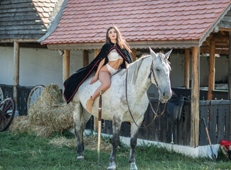 sensual brunette princess with sexy white bikinis riding a horse . Portrait of a girl  with cape and crown and her horse. Girl interacting and having fun with a horse in the  story fairytale style