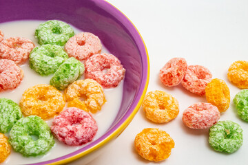Cereais coloridos dentro de uma vasilha com leite e alguns cereais caídos sobre a mesa.