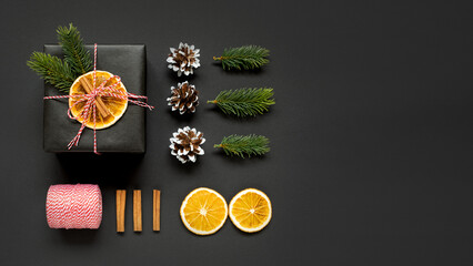Banner with black gift box with orange and spruce branches, cones and cinnamon on dark background