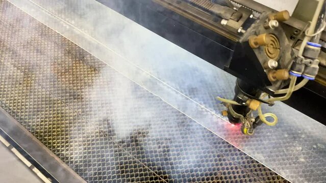 Cutting of polyethylene sheets on a machine with a red laser. Manufacture of PET parts. Production with acrid white smoke from the machine.