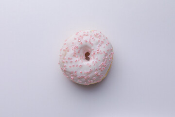 Ciambella con glassa e zuccherini rosa su superficie bianca