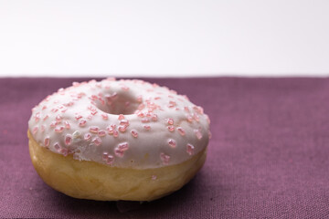 Ciambella con glassa e zuccherini rosa su superficie viola
