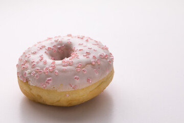 Ciambella con glassa e zuccherini rosa su superficie bianca