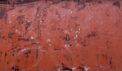 Front view of a messy, dirty and weathered plywood wall painted in red with stains from graffiti...