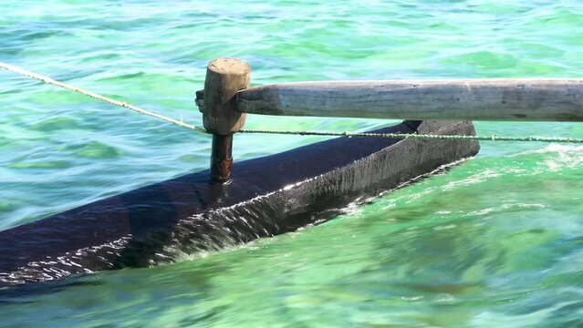 Looking to wooden pole and board of pirogue - typical Madagascar small fishing boat - sailing over clear green sea water