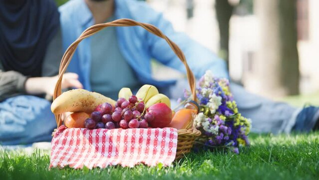 Picnic basket with fresh food on green grass, couple on romantic date in park