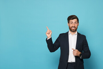 Smiling bearded man pointing index finger up on light blue background. Space for text