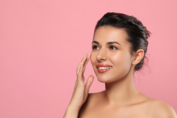 Woman applying cream under eyes on pink background, space for text. Skin care