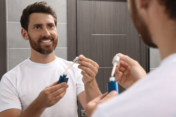 Handsome bearded man with bottle of oil in bathroom