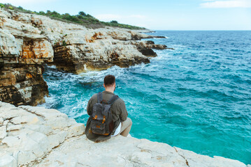 man with backpack sitting on the cliff enjoying city view