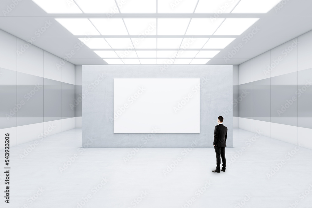 Poster Advertising concept with businessman back view in front of blank white poster with space for your logo or text on light grey concrete partition in abstract empty room, mockup