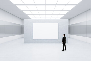 Advertising concept with businessman back view in front of blank white poster with space for your logo or text on light grey concrete partition in abstract empty room, mockup