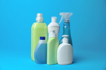 Many bottles of different detergents on light blue background. Cleaning supplies