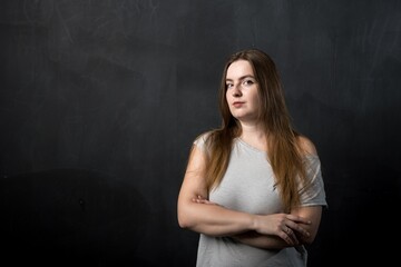 a woman of European appearance stands on a black background with folded hands.