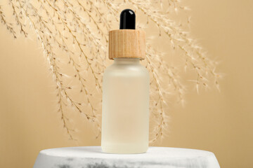 Bottle of face serum and dried flowers on marble stand against beige background, closeup