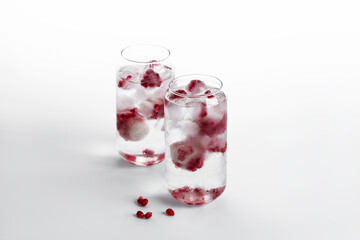 Glass of sparkling water with ice with pomegranate seeds on a white background for Valentine's day