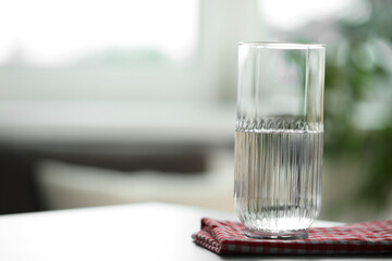 Glass of pure water on light table against blurred background, space for text