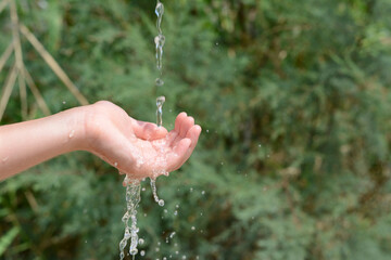 Pouring water into kid`s hand outdoors, closeup. Space for text