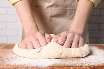 Woman kneading dough at wooden table near white brick wall, closeup