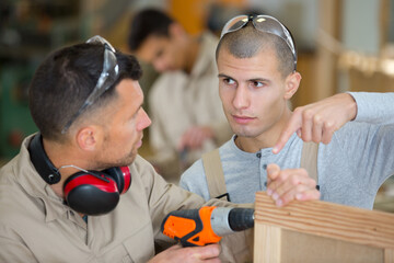 two men measuring detail and assembling product in carpentry workshop