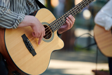 Man playing acoustic bass guitar at outdoor event, close up view to wooden guitar neck. Right...