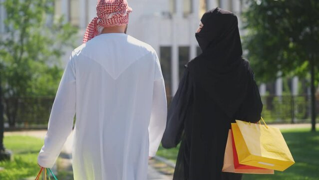 Arab couple in traditional Muslim clothing walking street with shopping bags