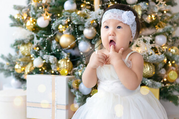 Merry Christmas and Happy New Year. A serious little child in a New Year's dress sits against the backdrop of a New Year's interior with a beautifully decorated Christmas tree.