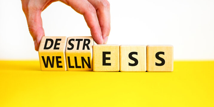 Destress for wellness symbol. Concept words Destress and Wellness on wooden cubes. Businessman hand. Beautiful yellow table white background. Business destress for wellness concept. Copy space.
