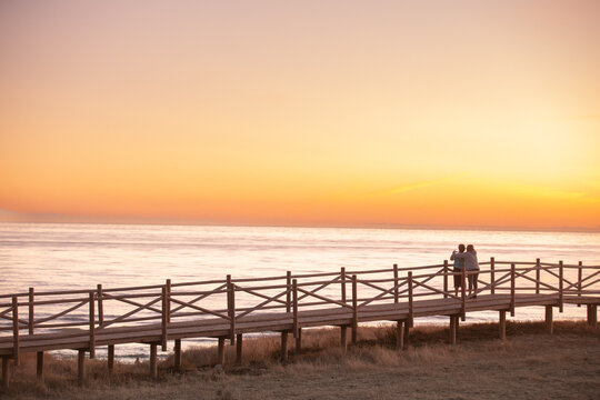 Personas abrazadas contemplando un atardecer en una playa de M&aacute;laga.