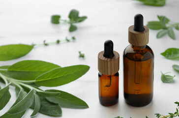 Bottles of essential oils and fresh herbs on white table, space for text