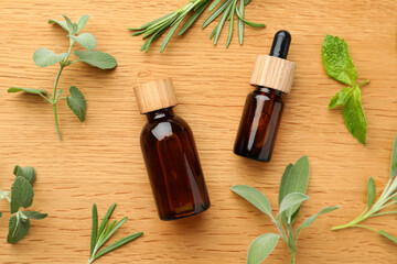 Bottles of essential oils and fresh herbs on wooden table, flat lay