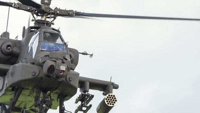 detailed close-up of British army Boeing Apache Attack helicopter gunship (AH-64E AH64E) flying slow and low, a glance from pilot and gunner, before Apache descends behind bushes