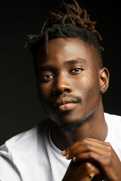 Dark studio portrait of black man in white shirt staring at camera