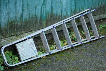 one white aluminum dirty folding ladder stepladder lies on gray asphalt in the street near the...