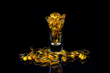 Fish oil capsules. Yellow omega 3 pills in jar on the dark black. fish oil capsules in wineglass...