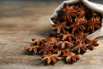 Overturned bag with aromatic anise stars on wooden table, closeup. Space for text