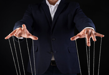 Man in suit pulling strings of puppet on black background, closeup - obrazy, fototapety, plakaty