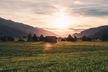 Diesiger Sonnenuntergang mit grüner Alpenwiese und Hütte im Vordergrund